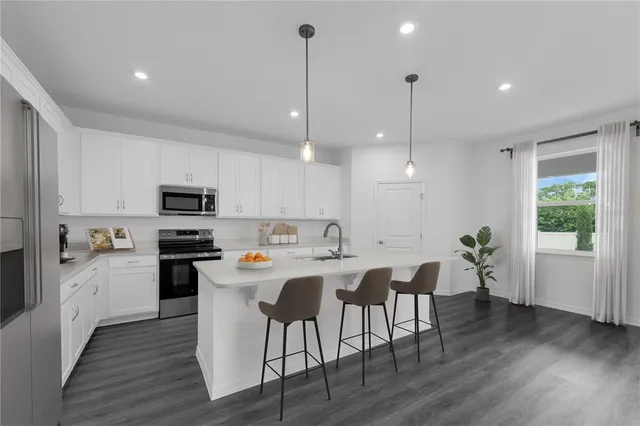 a kitchen with stainless steel appliances kitchen island granite countertop a stove a refrigerator a sink a dining table and chairs with wooden floor