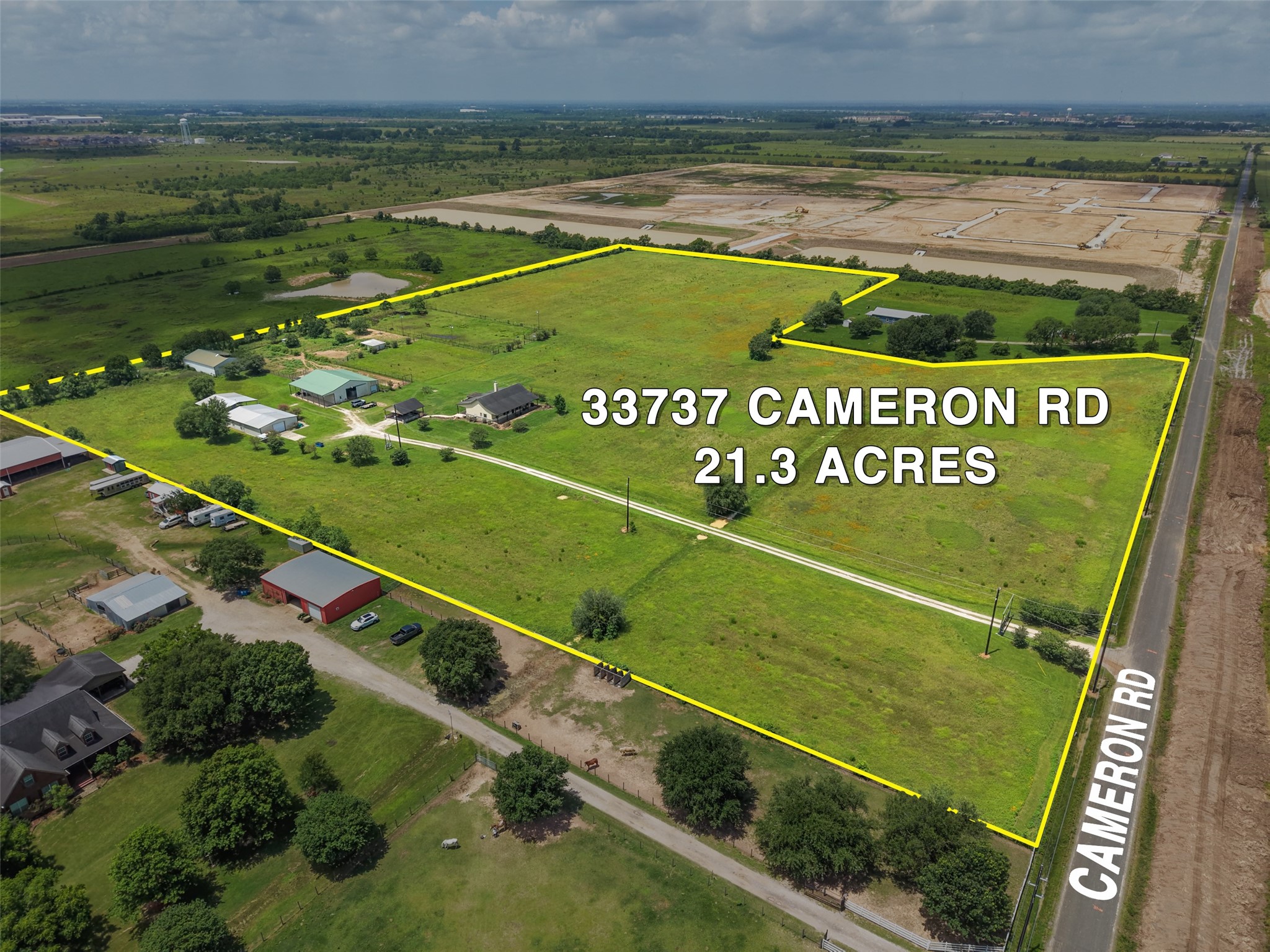 Expansive 21.3-acre property at 33737 Cameron Rd, featuring lush green fields, several buildings, and a clear boundary along a paved road, ideal for development or a spacious homestead.
