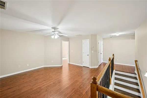 a view of an empty room with wooden floor and a ceiling fan