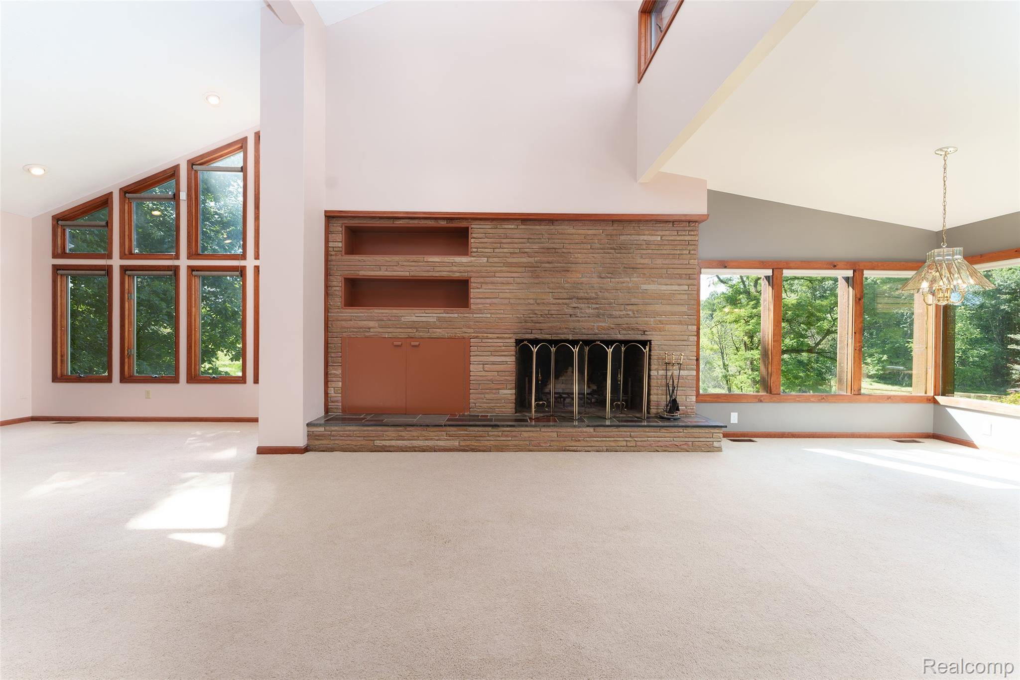 3166 Bigelow Road Howell, MI 48855 - Photo 8 of 50 Spacious living area featuring a stone fireplace with integrated built-in shelving, vaulted ceilings, and extensive window arrays with wood trim
