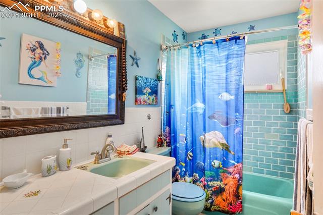 8155 Soap Weed Road Calhan, CO 80808 - Photo 20 of 39 Full bathroom with vanity, shower / bathtub combination with curtain, tile walls, toilet, and backsplash