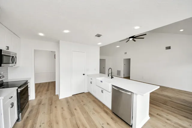 a large white kitchen with a stove a sink dishwasher and a refrigerator with wooden floor