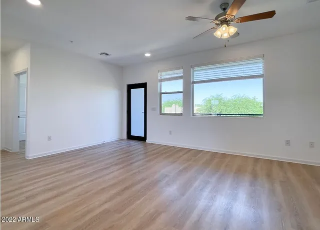 an empty room with wooden floor fan and windows
