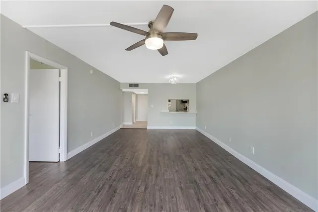 a view of an empty room with wooden floor and a ceiling fan