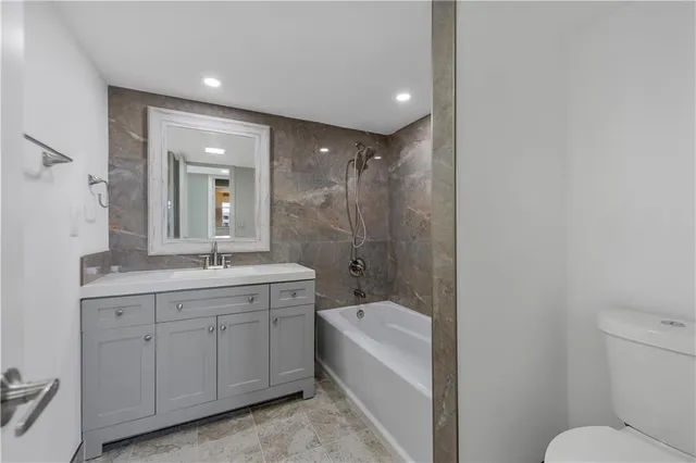 a bathroom with a granite countertop sink a toilet a mirror and bathtub