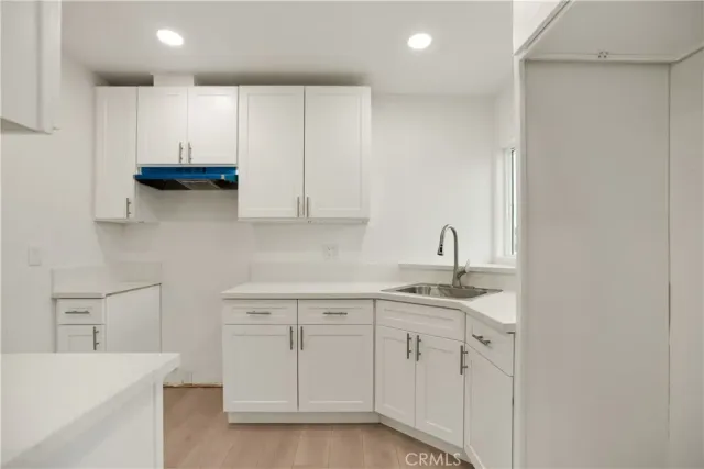 a kitchen with a sink dishwasher and white cabinets with wooden floor