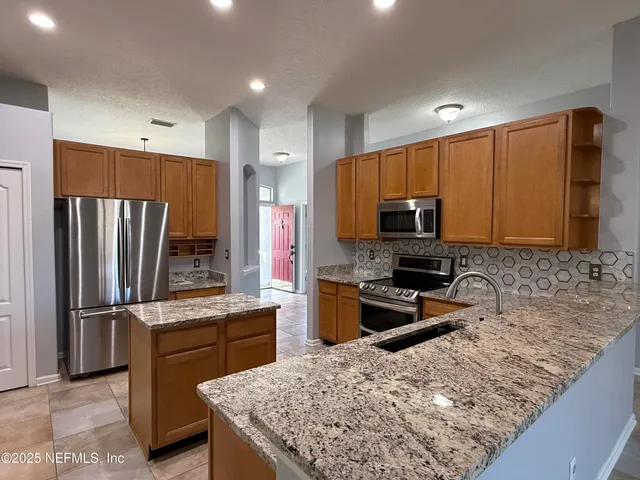 a kitchen with stainless steel appliances granite countertop wooden cabinets a stove a sink and a refrigerator
