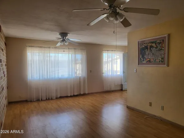 an empty room with wooden floor chandelier fan and windows