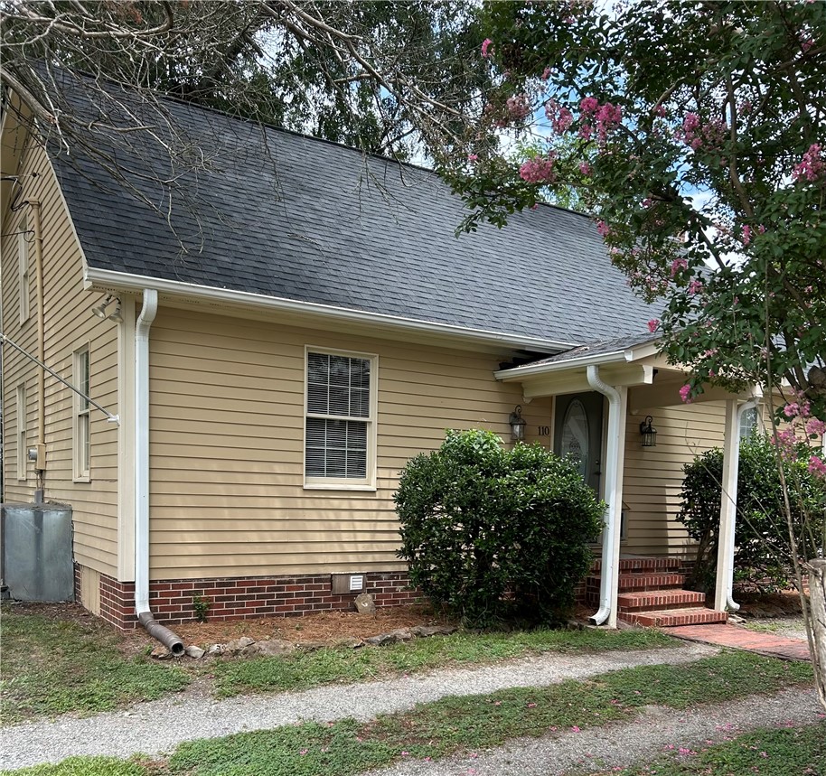 A charming residence with a covered front porch, brick stairs, and verdant landscaping.