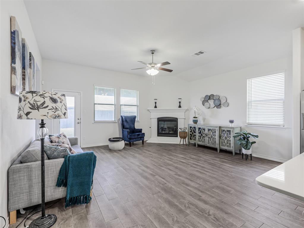 3024 Meredith Lane Forney, TX 75126 - Photo 7 of 29 Open-concept living space featuring wood-finish flooring, a corner fireplace with a white mantel, and a ceiling fan