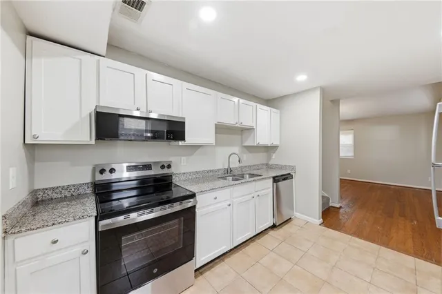 a kitchen with stainless steel appliances granite countertop white cabinets a sink a stove a microwave and a refrigerator