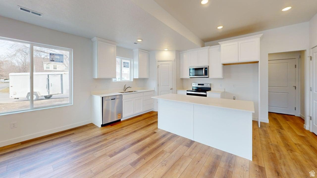 783 Pheasantbrook Drive, Unit 2A Centerville, UT 84014 - Photo 8 of 41 Modern kitchen featuring wood-finish flooring, white cabinetry, a central island, stainless steel dishwasher, and an over-range microwave