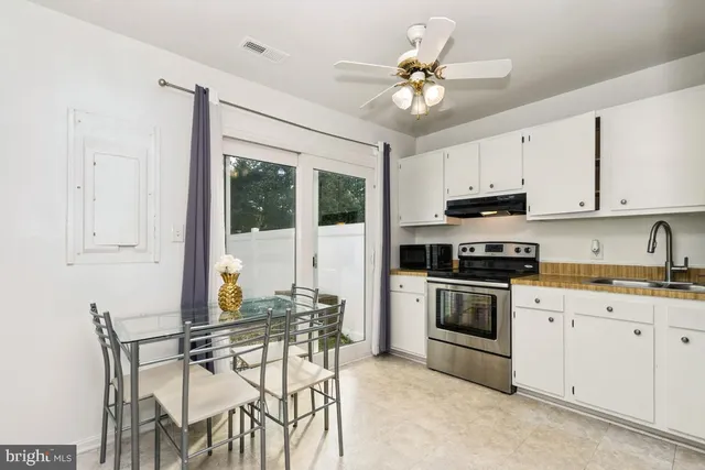 a kitchen with stainless steel appliances granite countertop a stove top oven a sink a dining table and chairs with white cabinets