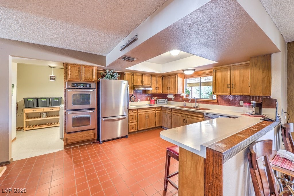 10615 Rancho Destino Road Las Vegas, NV 89183 - Photo 14 of 53 Kitchen featuring visible vents, a peninsula, a kitchen breakfast bar, stainless steel appliances, and a raised ceiling