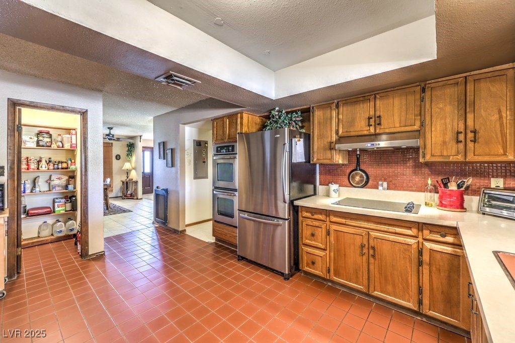 10615 Rancho Destino Road Las Vegas, NV 89183 - Photo 17 of 53 Kitchen featuring under cabinet range hood, brown cabinets, appliances with stainless steel finishes, and light countertops