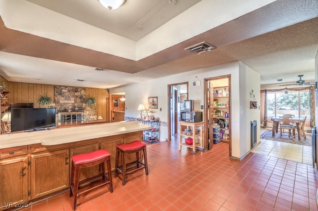 10615 Rancho Destino Road Las Vegas, NV 89183 - Photo 18 of 53 Kitchen featuring visible vents, a breakfast bar, a textured ceiling, wood walls, and brown cabinetry
