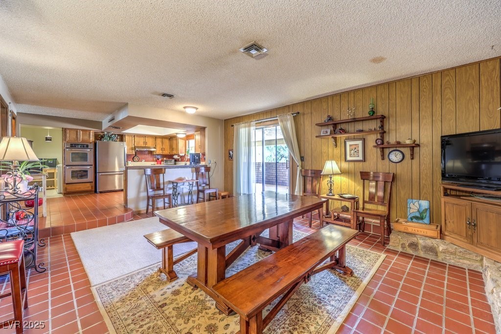 10615 Rancho Destino Road Las Vegas, NV 89183 - Photo 19 of 53 Dining room featuring tile patterned floors, visible vents, wood walls, and a textured ceiling