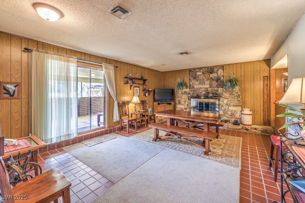 10615 Rancho Destino Road Las Vegas, NV 89183 - Photo 20 of 53 Tiled living room featuring visible vents, a textured ceiling, a stone fireplace, and wooden walls