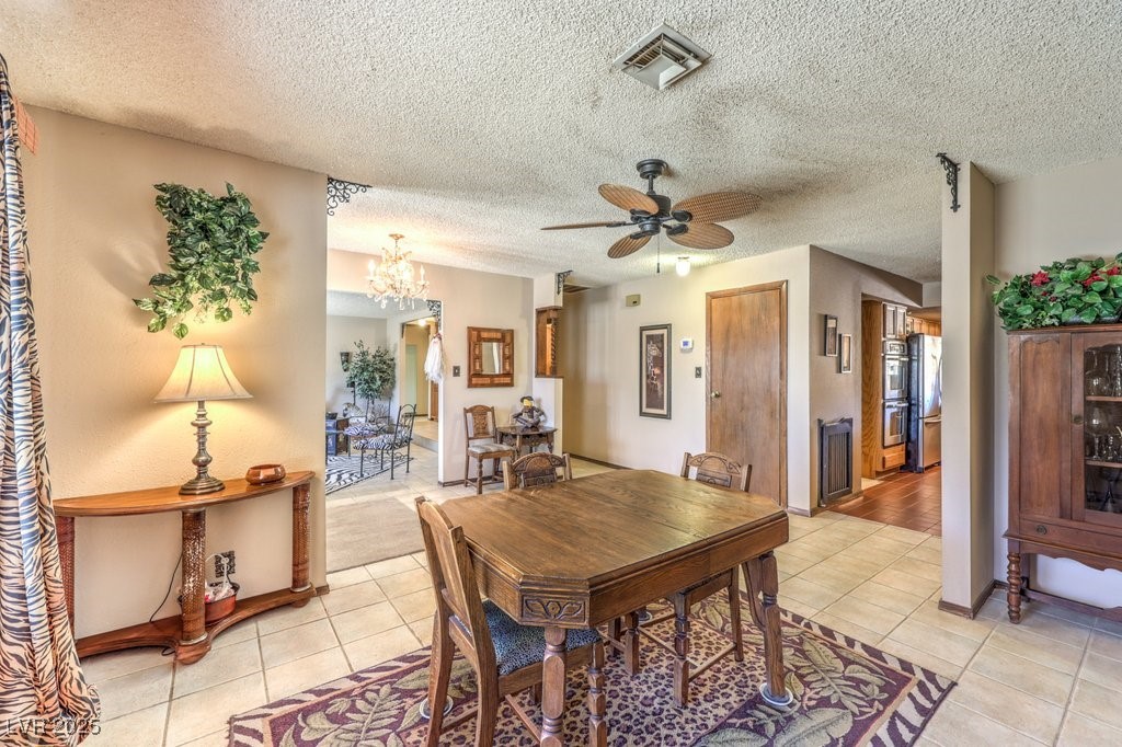 10615 Rancho Destino Road Las Vegas, NV 89183 - Photo 9 of 53 Dining room with light tile patterned floors, visible vents, a textured ceiling, and ceiling fan with notable chandelier