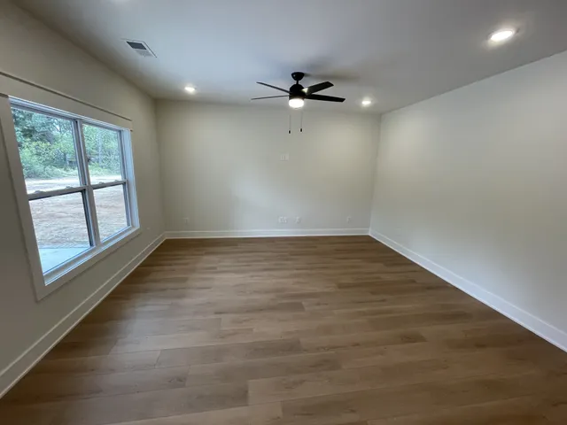 an empty room with wooden floor fan and windows