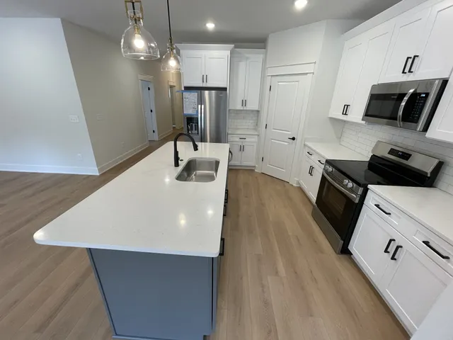 a kitchen with stainless steel appliances a refrigerator a sink a stove and white cabinets