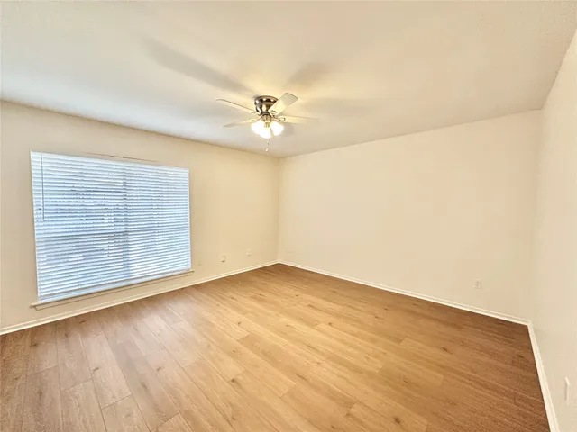 an empty room with wooden floor chandelier fan and windows