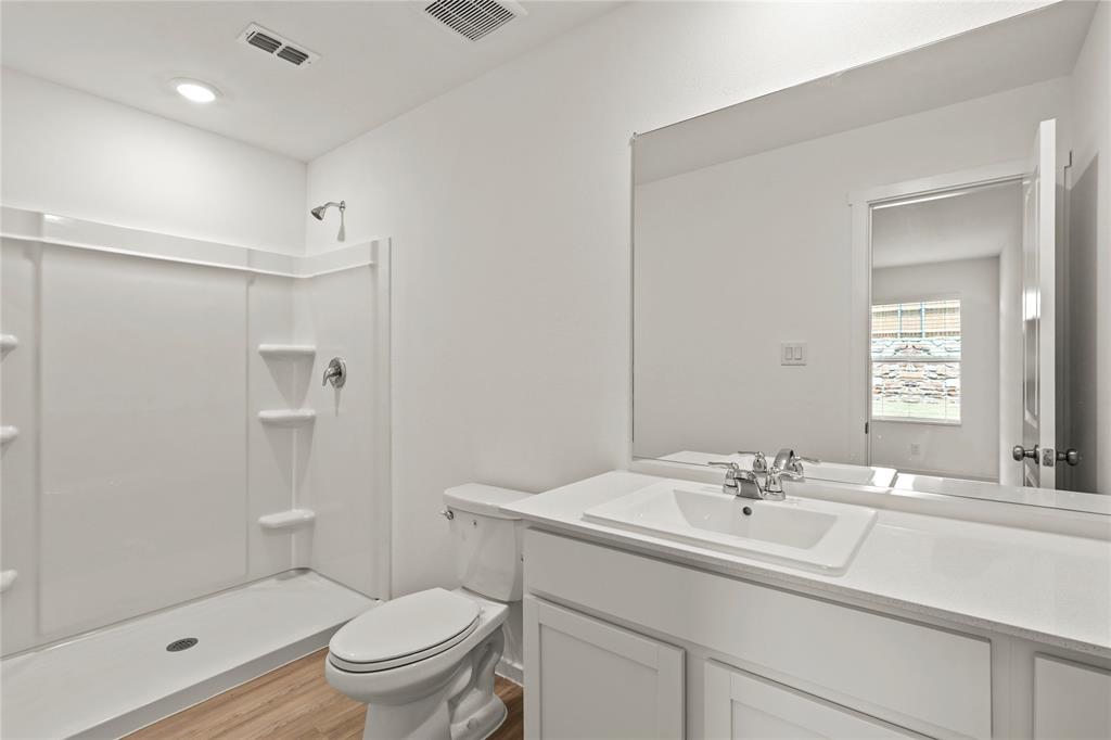 1138 Barbary Flds Street Forney, TX 75126 - Photo 16 of 25 Full bathroom featuring a single-basin vanity with a white countertop, a large wall-mounted mirror, a commode, a shower enclosure, and wood-finish flooring