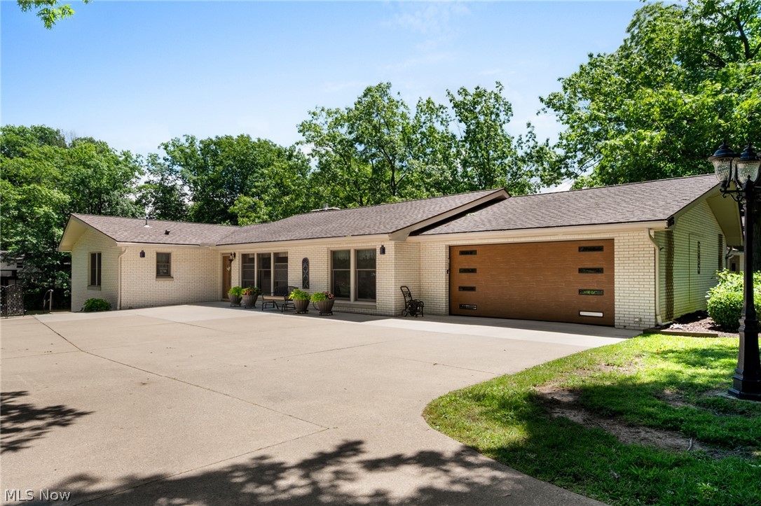 White brick exterior with a brown shingle roof and a large concrete driveway