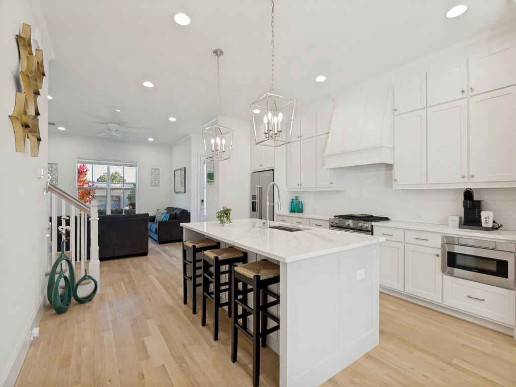 732 West 7th Street Dallas, TX 75208 - Photo 9 of 25 Open-concept kitchen featuring an oversized island with seating, white shaker cabinetry, stainless steel appliances, and wood-finish flooring throughout