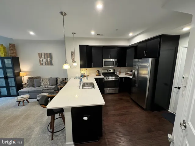 a living room with stainless steel appliances furniture a rug and a view of kitchen