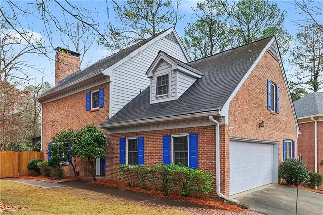 a view of a house with brick walls plants and large tree