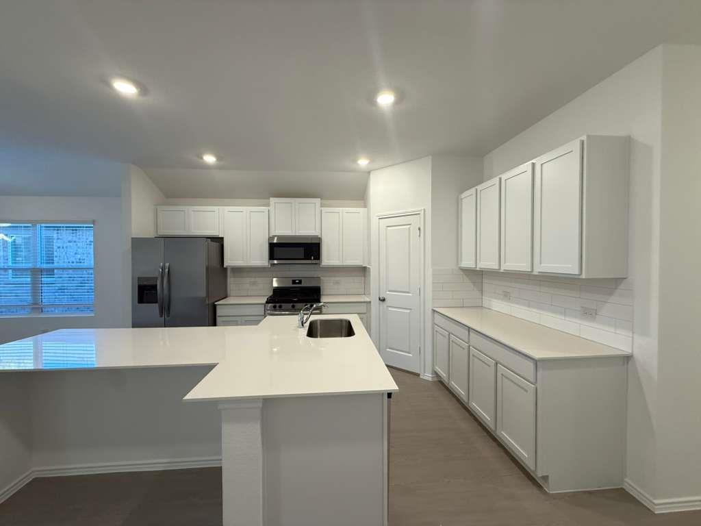 545 Sormonne Loop Kyle, TX 78640 - Photo 13 of 39 Kitchen featuring stainless steel appliances, a center island with sink, decorative backsplash, white cabinets, and dark wood-style flooring