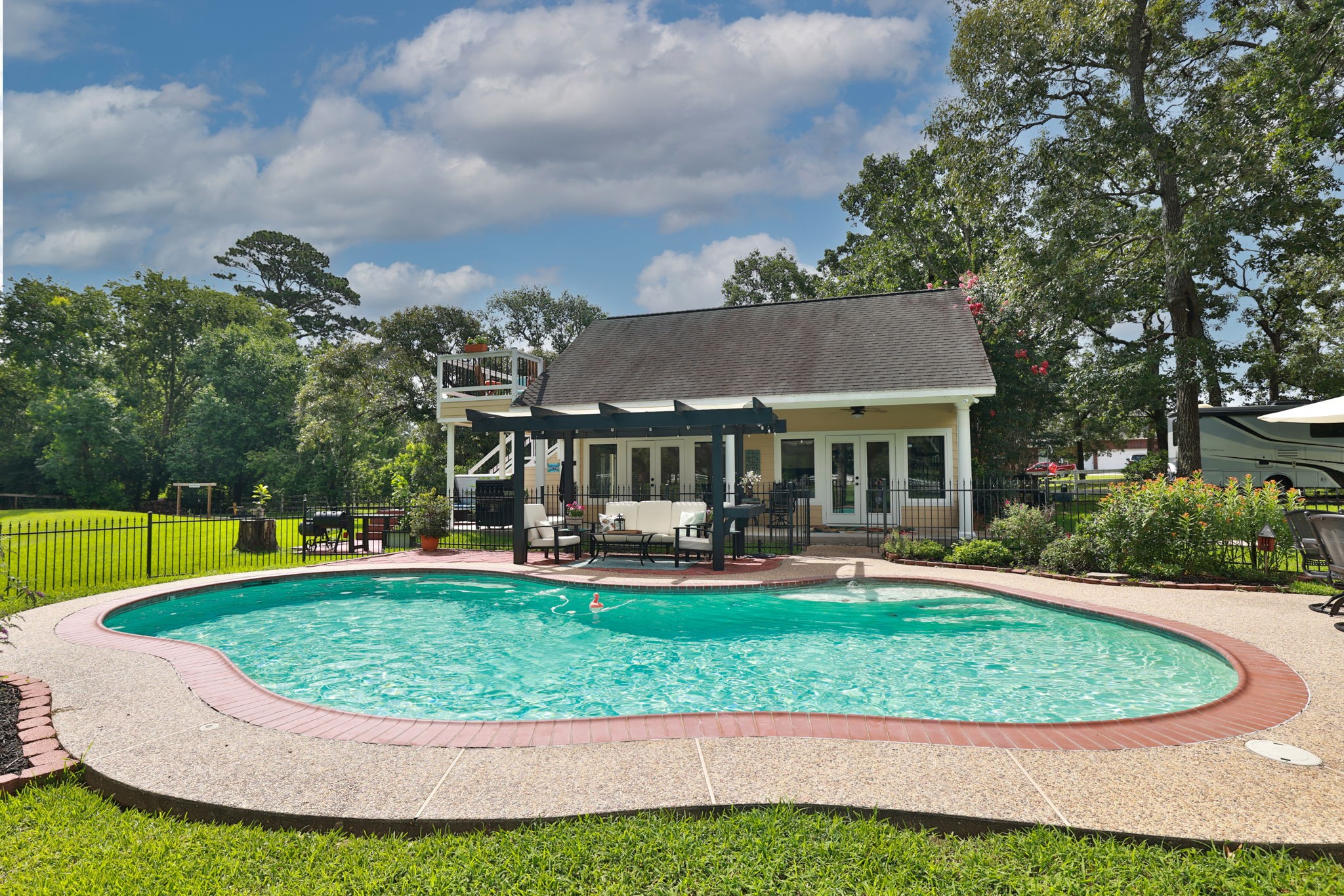 34310 High Point Drive Magnolia, TX 77355 - Photo 39 of 48 This photo showcases a charming backyard with a kidney-shaped pool, surrounded by a well-maintained lawn and a cozy patio area. The guest house has a rustic design with a pergola for outdoor relaxation, and mature trees provide shade and privacy. Ideal for summer entertaining.