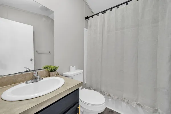 a bathroom with a granite countertop sink toilet a mirror and shower curtain
