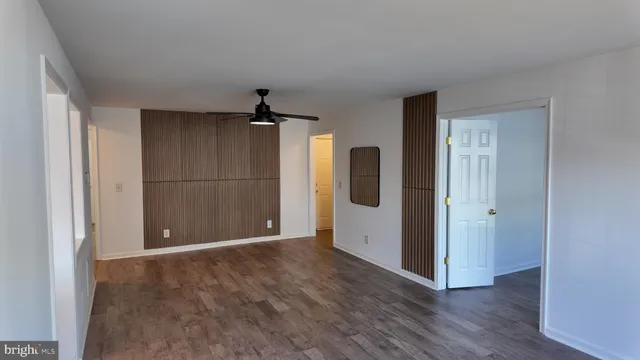 a view of an empty room with wooden floor and a ceiling fan