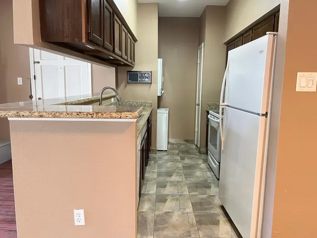 a kitchen with stainless steel appliances granite countertop a refrigerator a stove and a sink with wooden cabinets