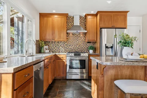 a kitchen with stainless steel appliances granite countertop a stove and a view of living room