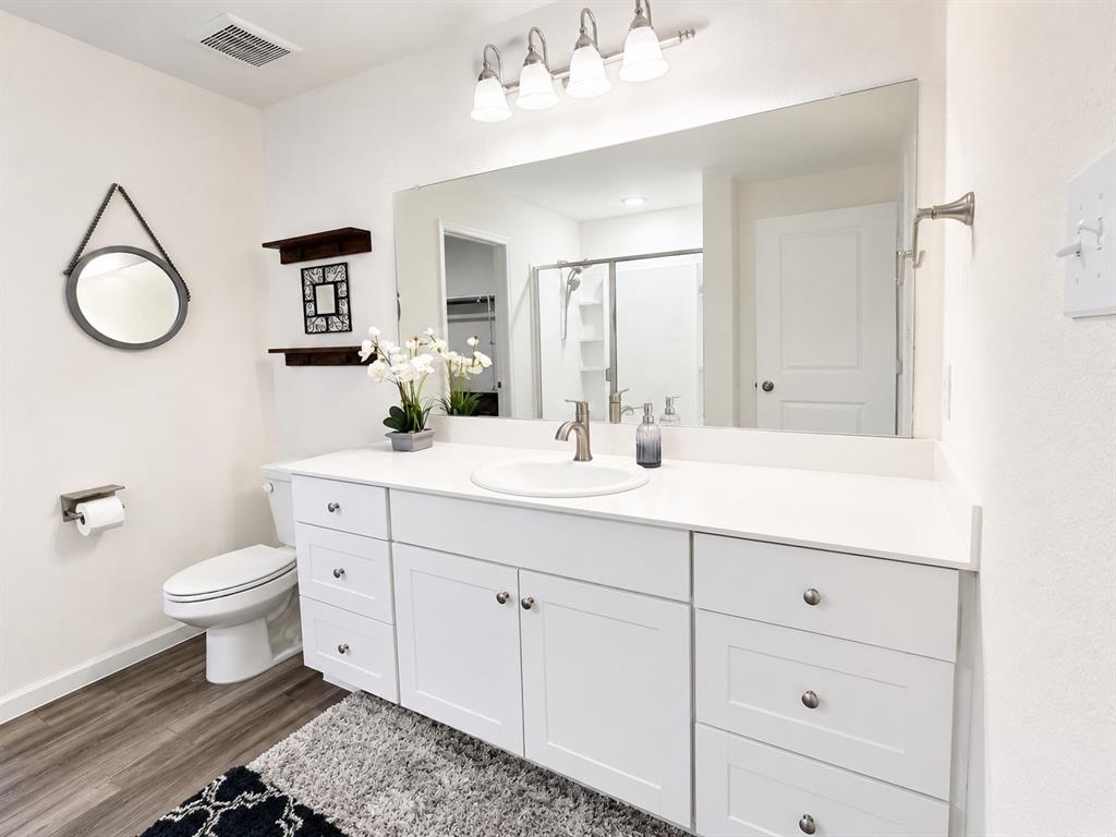824 Juniper Street Anna, TX 75409 - Photo 17 of 25 Bathroom featuring a white vanity with extensive storage, a large wall-mounted mirror, brushed nickel fixtures, a toilet, and wood-finish flooring