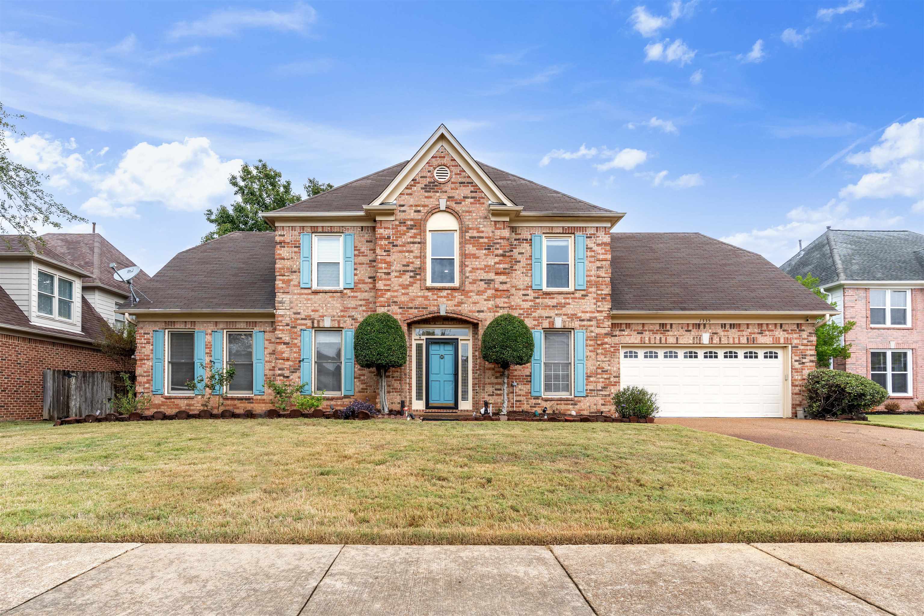 Colonial inspired home with a shingled roof, brick siding, a front lawn, and driveway
