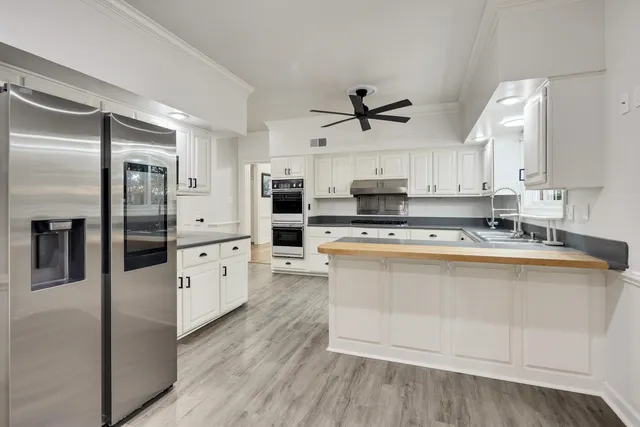 a large kitchen with stainless steel appliances a refrigerator a stove a microwave and white cabinets