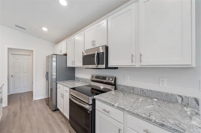 a kitchen with stainless steel appliances granite countertop a refrigerator stove and white cabinets with wooden floor