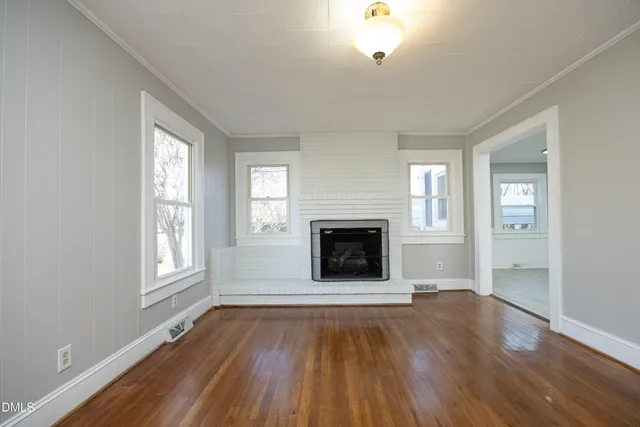 an empty room with windows a fireplace and wooden floor