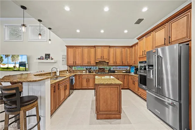 a kitchen with stainless steel appliances granite countertop a refrigerator a sink dishwasher a stove top oven a kitchen island and chairs with wooden floor