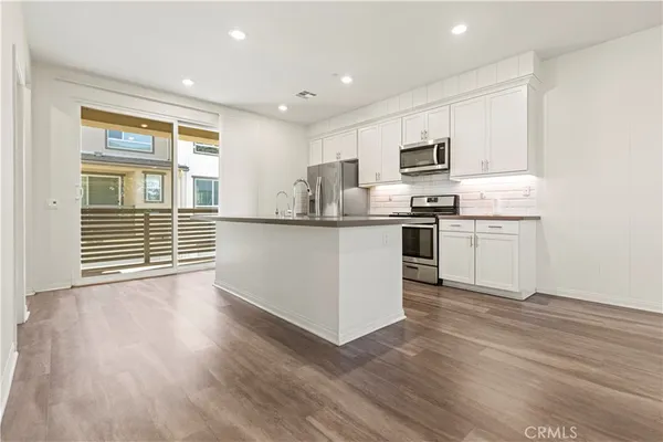 a kitchen with stainless steel appliances granite countertop a stove top oven a sink dishwasher and a refrigerator with wooden floor
