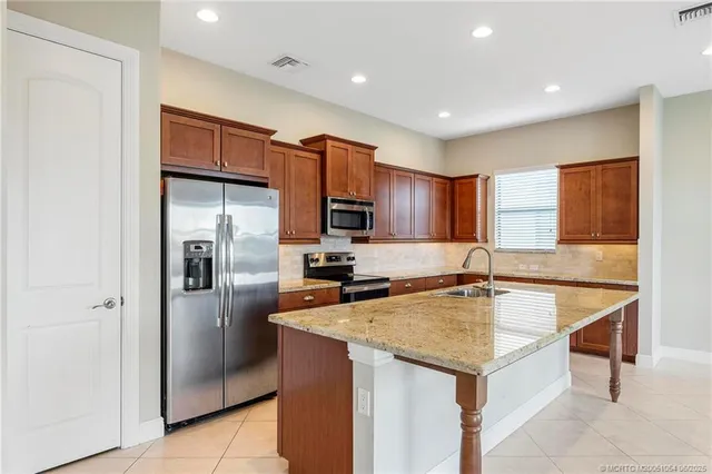 a kitchen with stainless steel appliances granite countertop a sink a refrigerator and a stove top oven with wooden floor