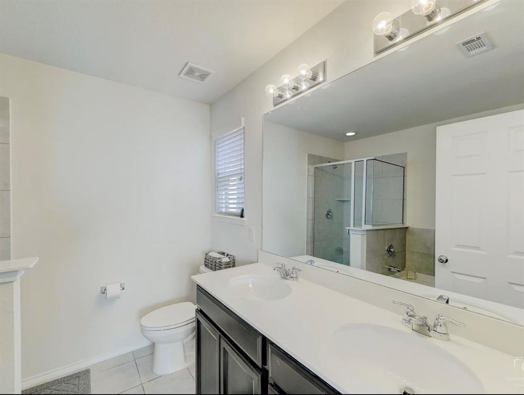 2207 Heaton Street Forney, TX 75126 - Photo 18 of 25 Bathroom featuring a double vanity with undermount sinks, a large wall-mounted mirror, a separate glass-enclosed shower, a toilet, and a window with blinds