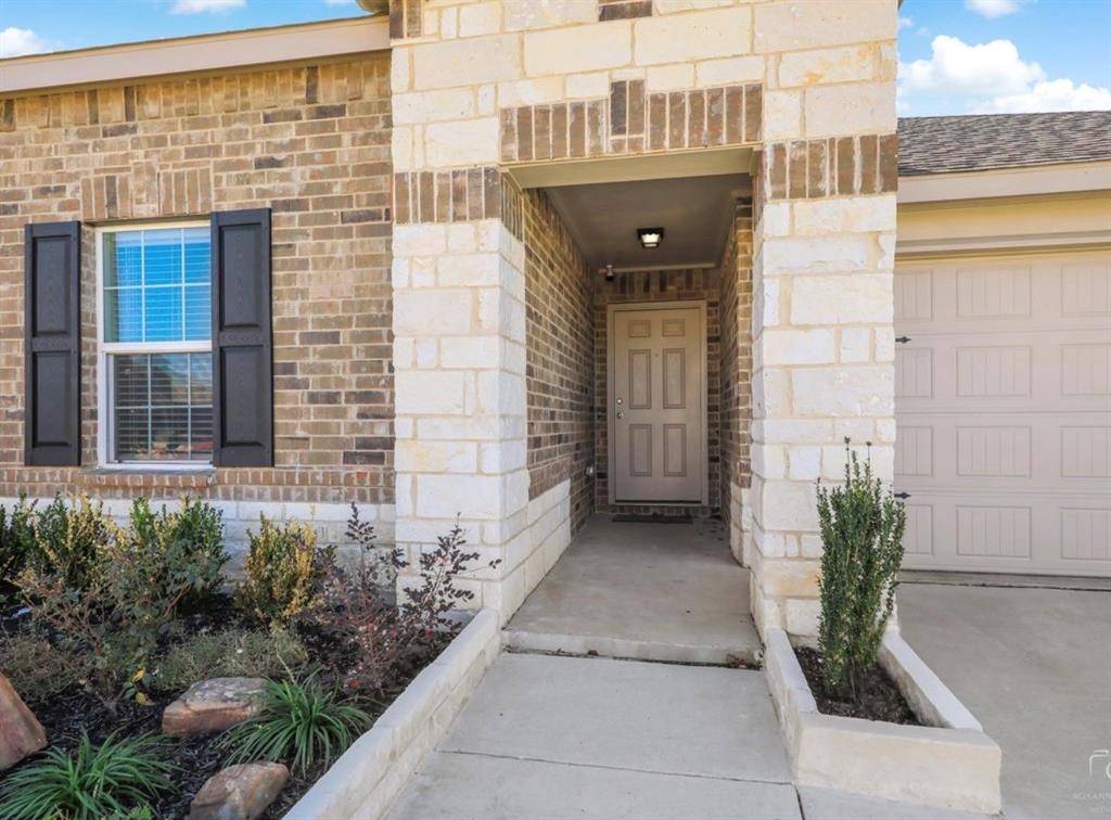 2207 Heaton Street Forney, TX 75126 - Photo 2 of 25 Brick and stone facade featuring a recessed entry, panel garage door, and a planted landscape bed with natural rock accents