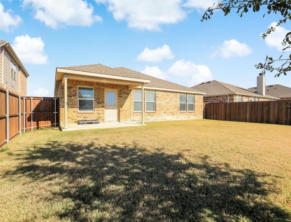 2207 Heaton Street Forney, TX 75126 - Photo 25 of 25 Expansive backyard with a manicured lawn, brick exterior, covered patio, and wood privacy fencing