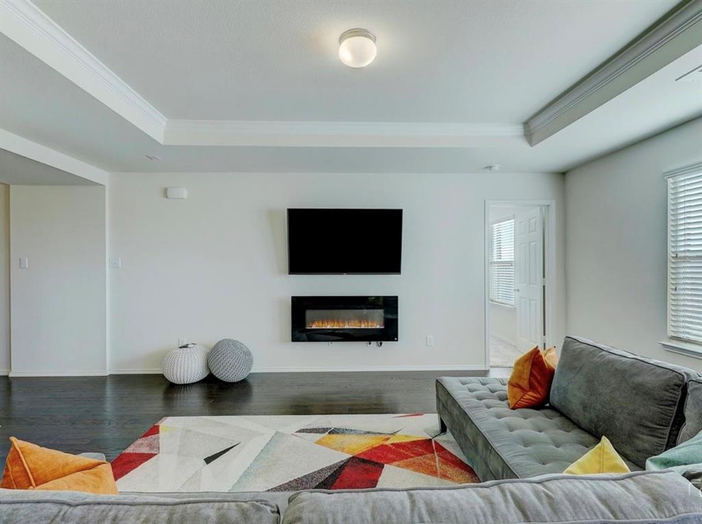 2207 Heaton Street Forney, TX 75126 - Photo 6 of 25 Living area featuring a modern wall-mounted fireplace, dark wood-finish flooring, and tray ceilings with crown molding