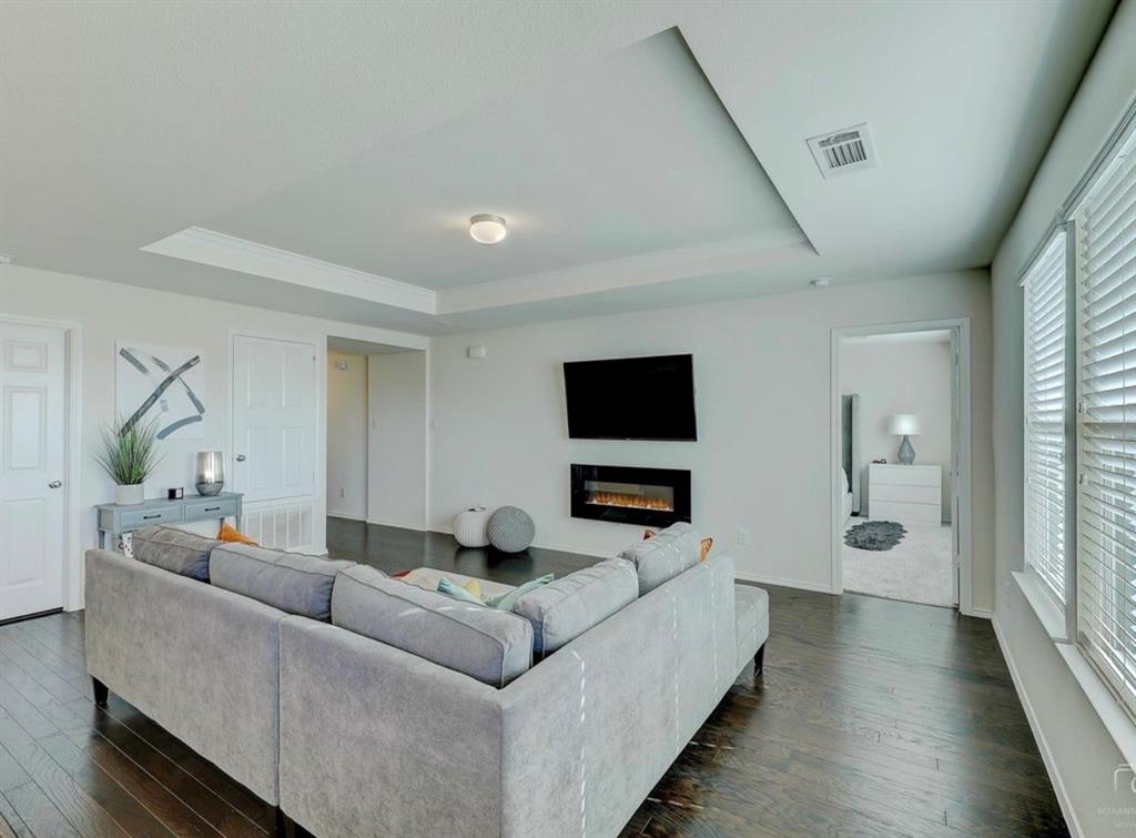 2207 Heaton Street Forney, TX 75126 - Photo 7 of 25 Spacious living area featuring dark wood-finish flooring, a contemporary electric fireplace, and a tray ceiling with recessed lighting